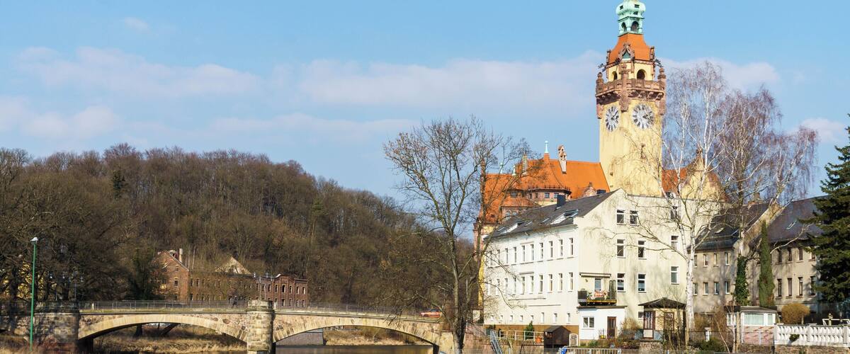A stone bridge over a river, a clock tower, and a building with a red roof.