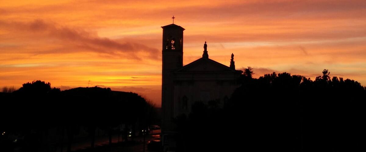 A sunset over a cityscape with a prominent church tower silhouetted against a vibrant sky.