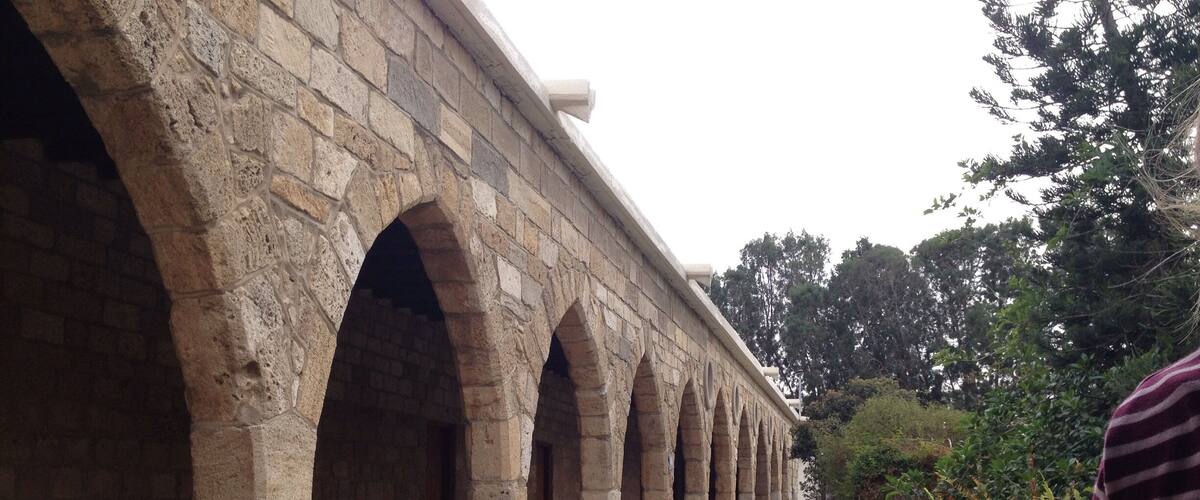 An ancient stone bridge with multiple arches, a stone pathway, and lush greenery in the background.