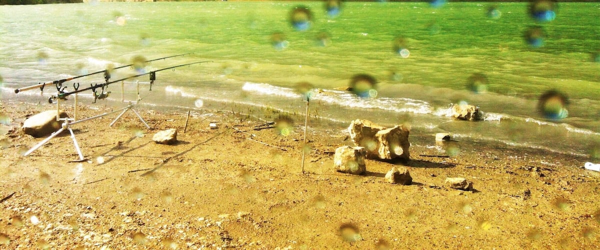 A beach with fishing rods and rocks, clear water, and hills in the background.