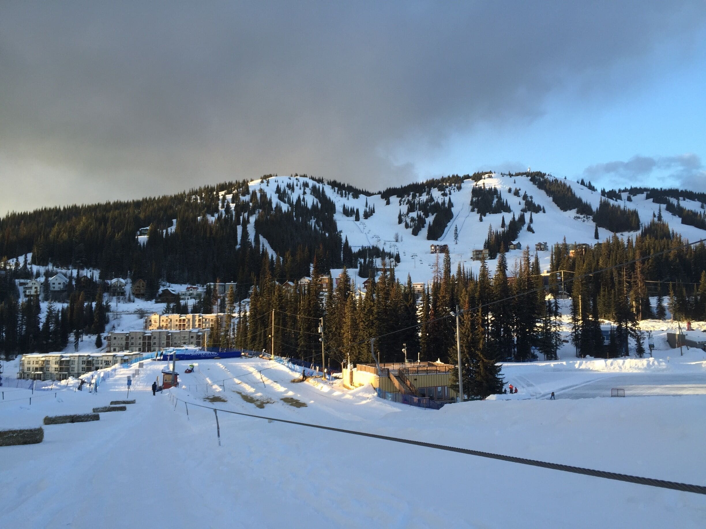 A snow-covered ski slope with buildings and trees in the background.