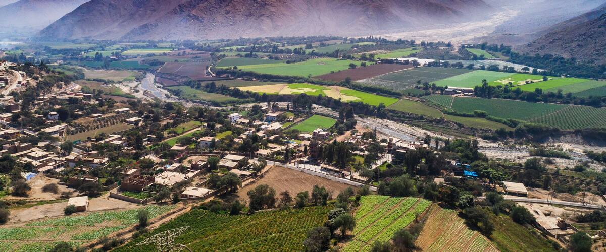 A mountainous landscape with a valley, agricultural fields, and a small village.