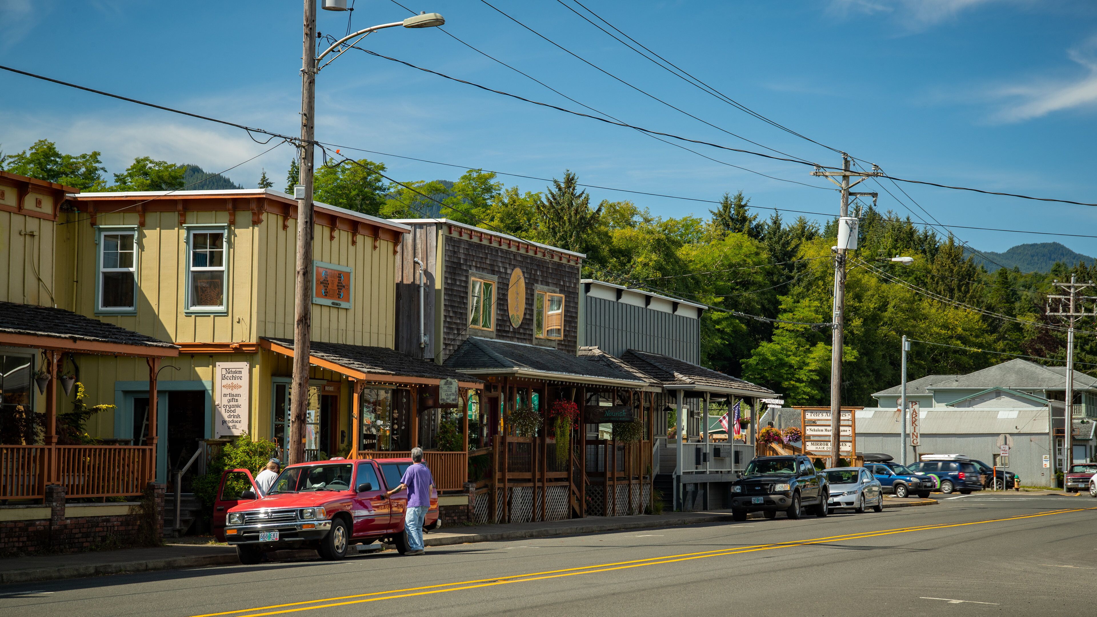 A street lined with wooden buildings, a red truck parked on the side, and a clear blue sky.