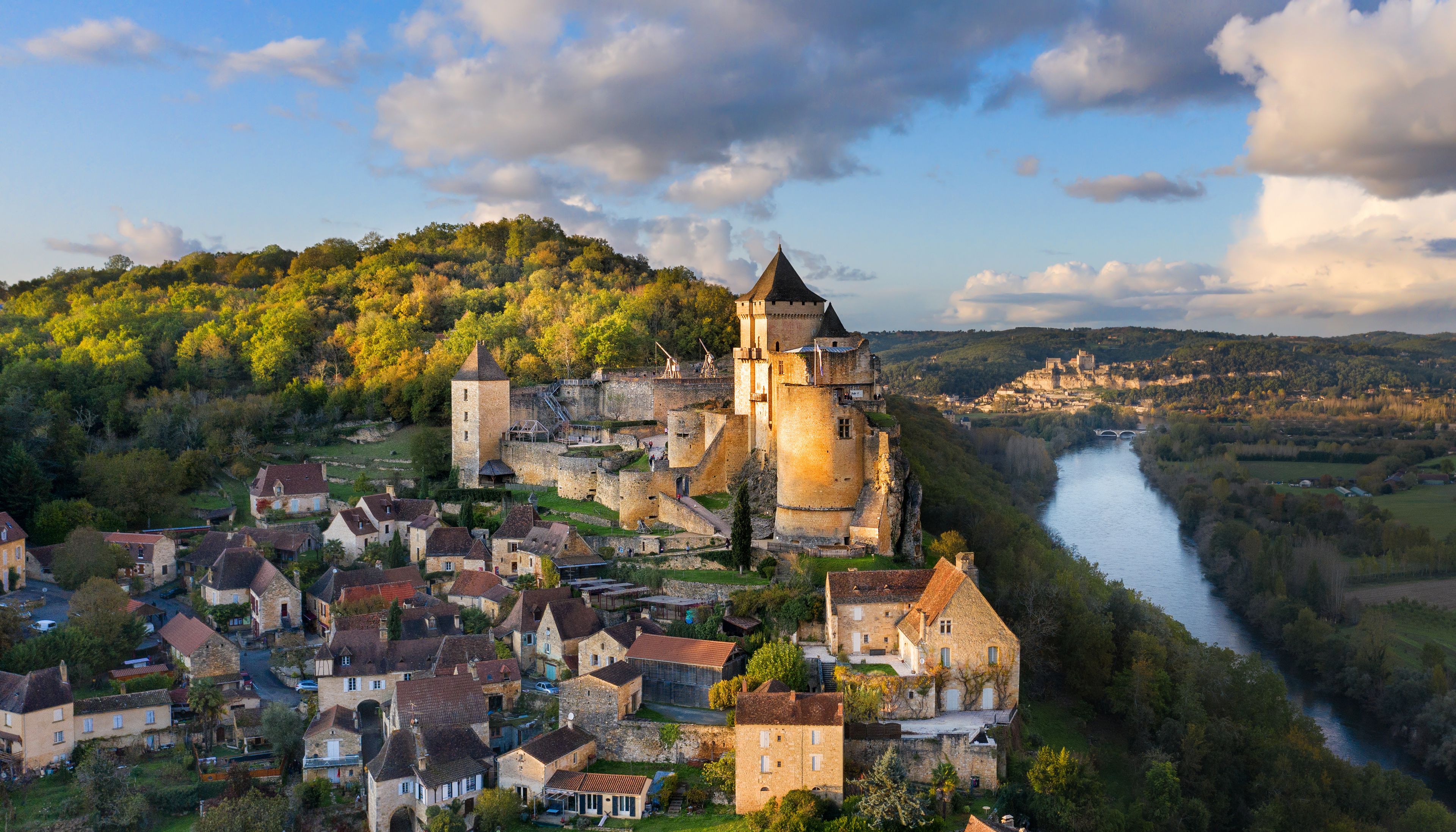 A historic castle on a hill overlooking a river, surrounded by a small town with traditional architecture.