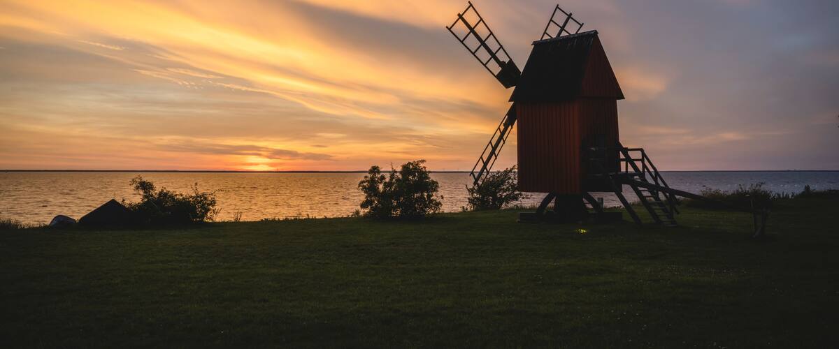 Un molino de viento al atardecer con un mar tranquilo al fondo.