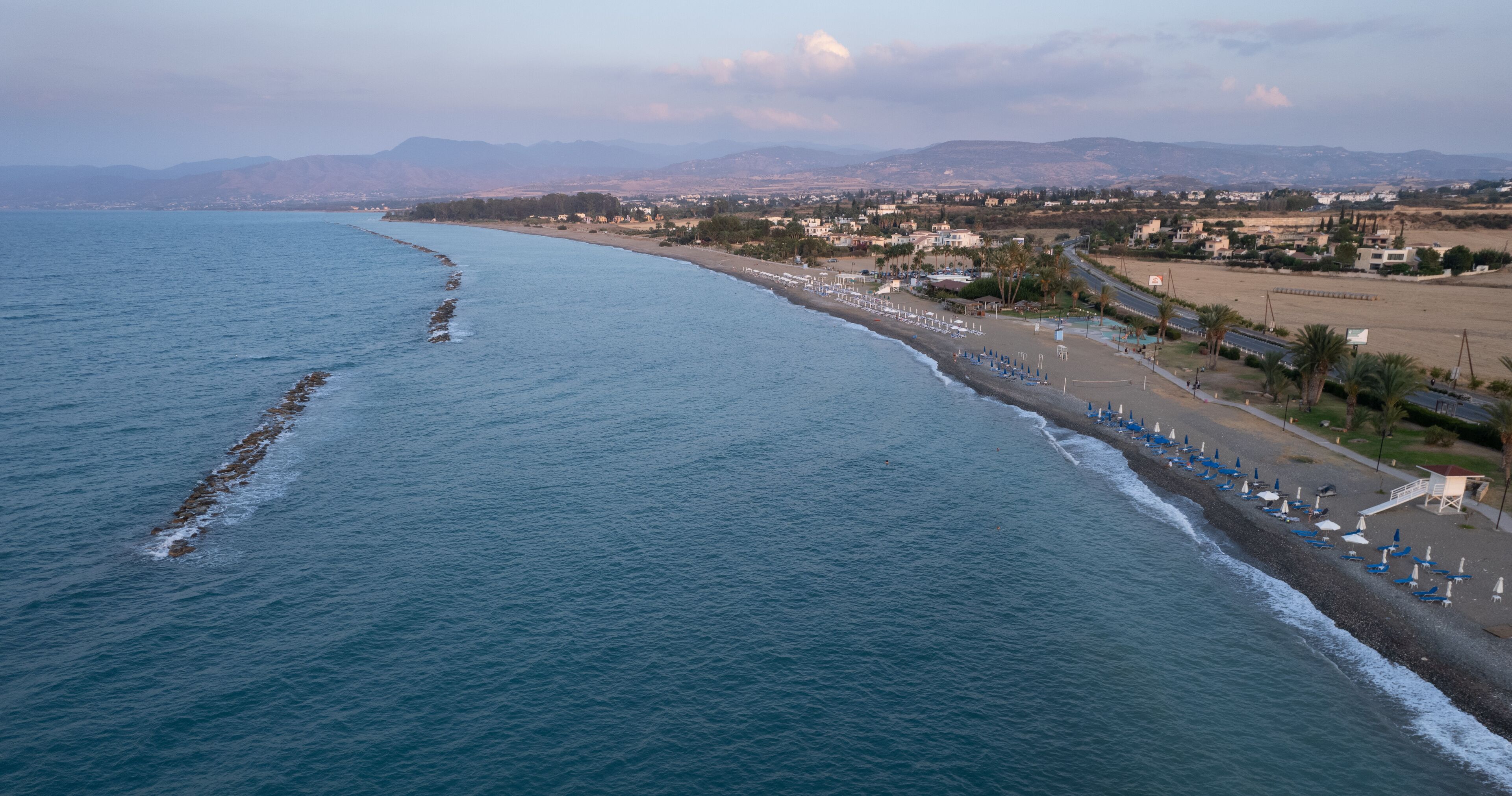 A coastal landscape with a beach, ocean, and distant mountains.