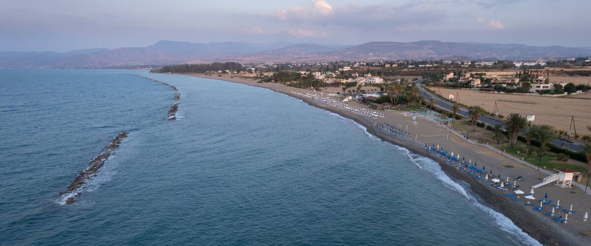 A coastal landscape with a beach, ocean, and distant mountains.