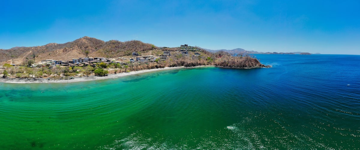 An aerial view of a coastal town with buildings on a hillside and a beach.
