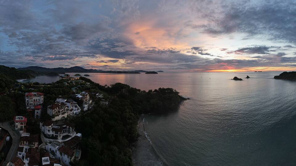 A coastal landscape with a sunset, a calm sea, and a densely built town on the hills.