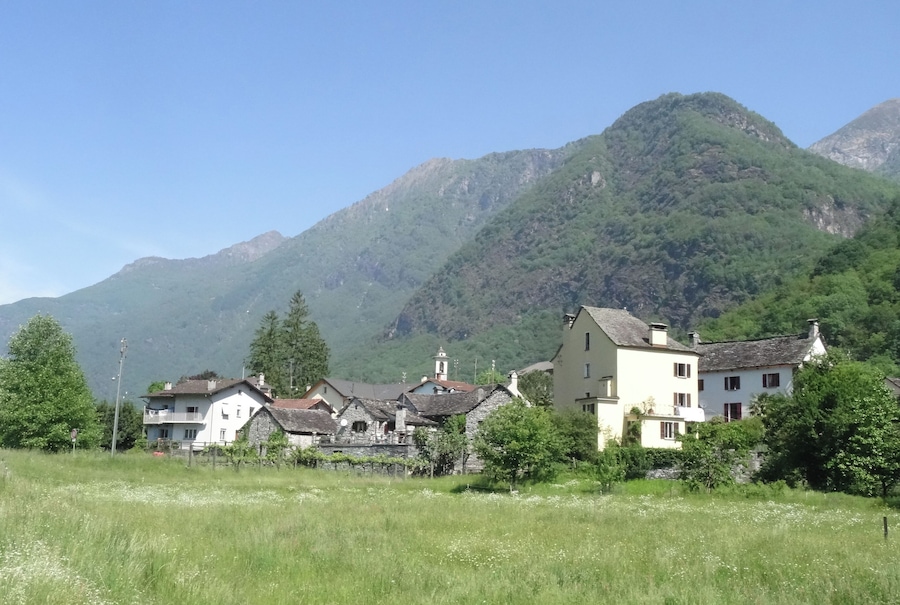 A village with traditional houses, a church, and mountains in the background.
