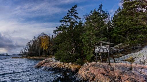 Une côte rocheuse, avec un panneau en bois indiquant « SODRA GRINDA », au milieu d’une forêt dense et près d’une étendue d’eau.