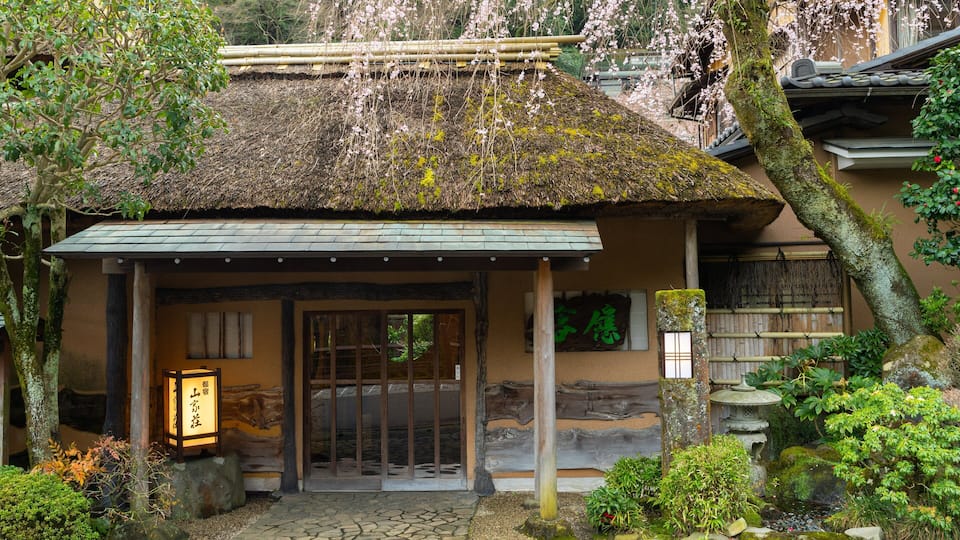 A traditional Japanese building with a thatched roof, wooden pillars, and a stone pathway leading to the entrance.