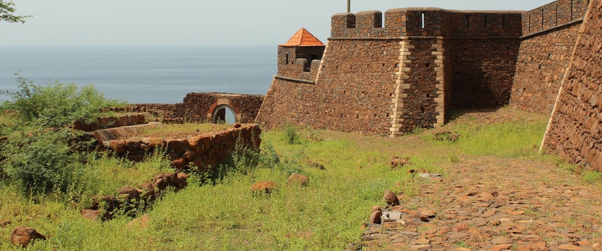 A stone fort with a flag, a small tower, and a view of the sea.