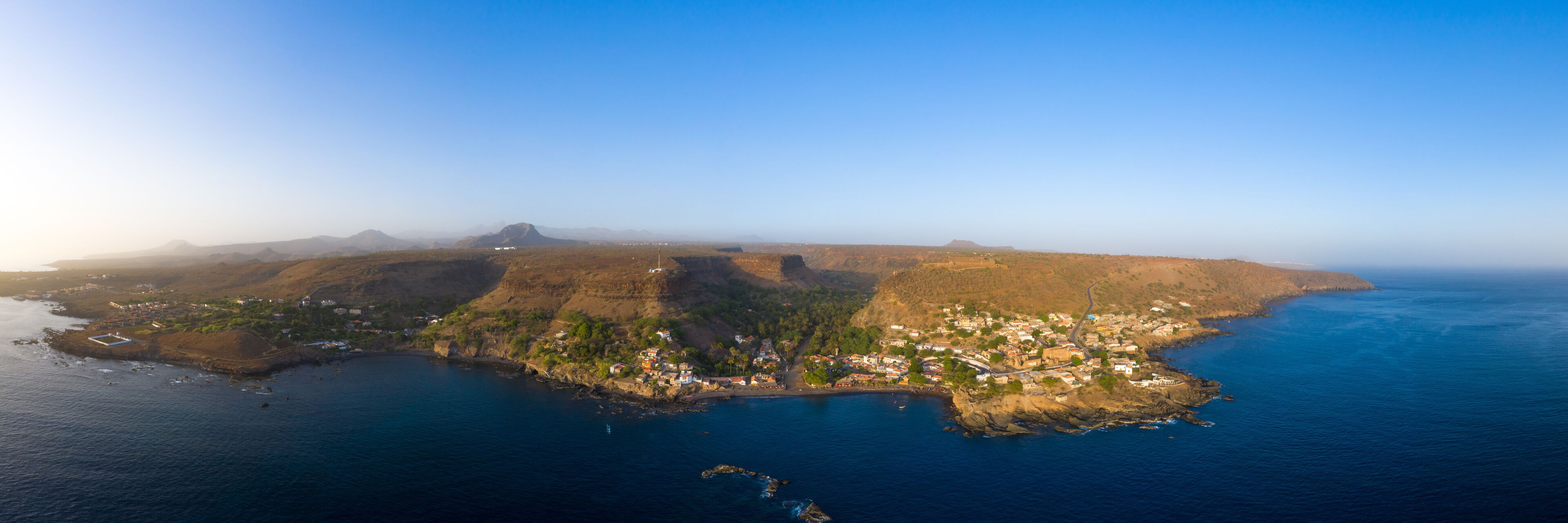 An aerial view of a coastal town with a rugged coastline, a bay, and distant mountains.
