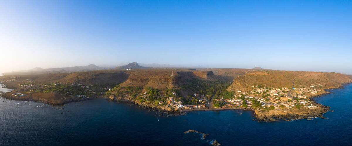 An aerial view of a coastal town with a rugged coastline, a bay, and distant mountains.