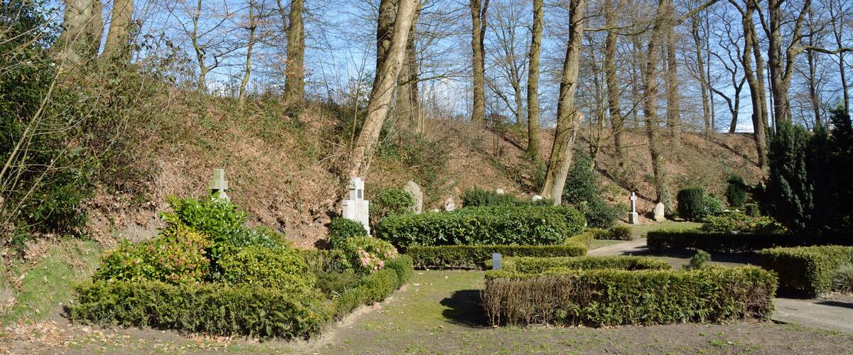 A cemetery with neatly trimmed hedges and a variety of tombstones.