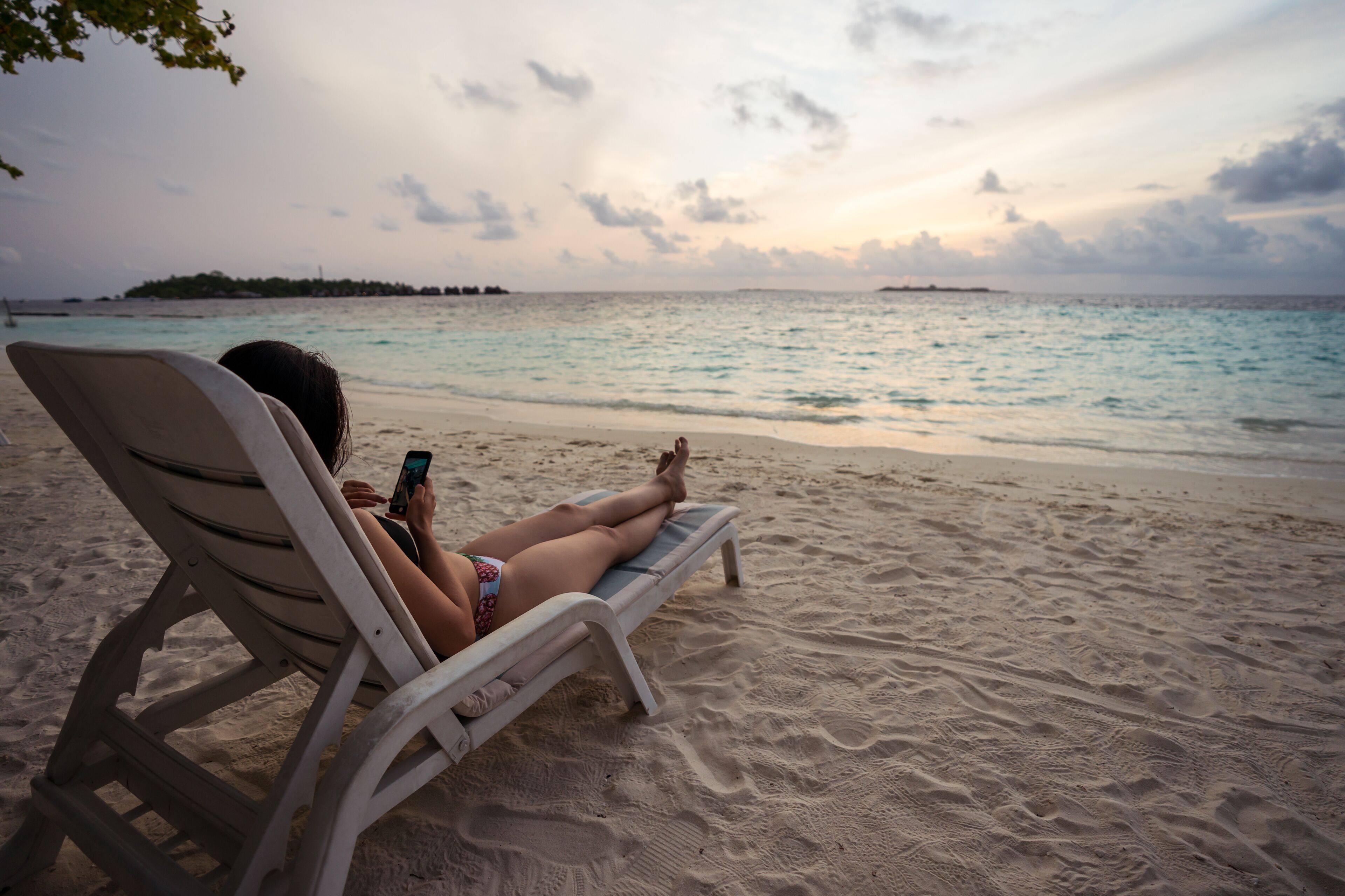 A person relaxing on a beach chair, looking at a smartphone.