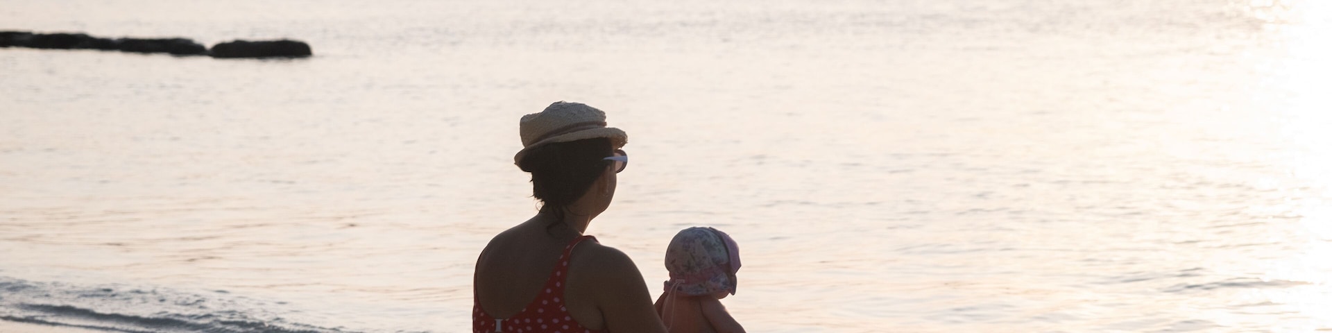 Una mujer y un niño sentados en la playa con una fila de casas al fondo.