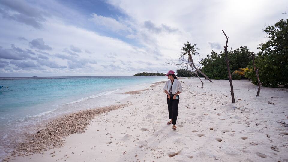 A sandy beach with footprints, palm trees, and a calm sea under a cloudy sky.