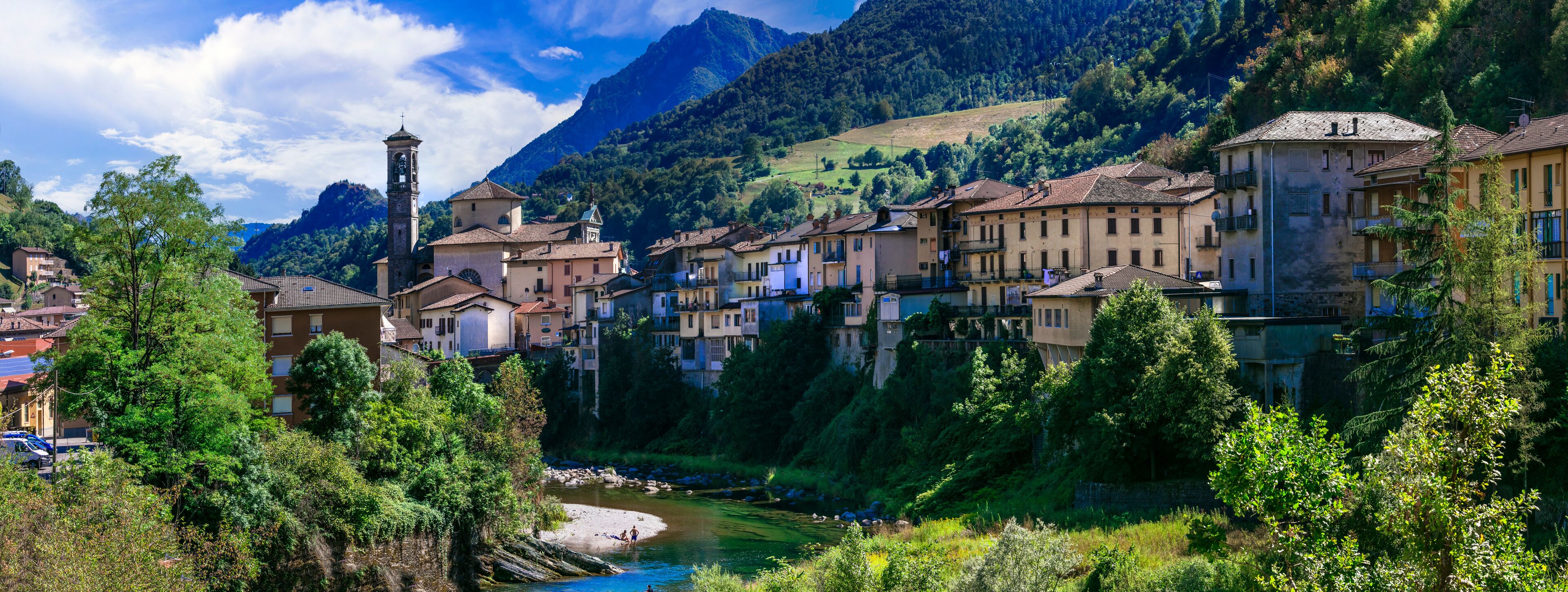 A picturesque village with a river, surrounded by lush greenery and mountains.