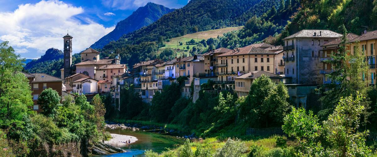 A picturesque village with a river, surrounded by lush greenery and mountains.