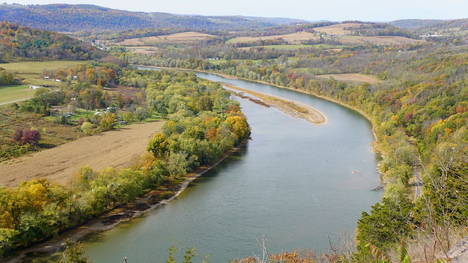 A river winding through a valley with autumn foliage, surrounded by hills and scattered houses.