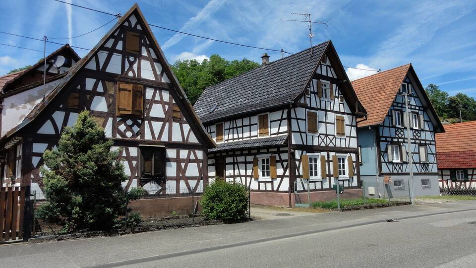 A row of traditional half-timbered houses with a clear sky and a road in front.