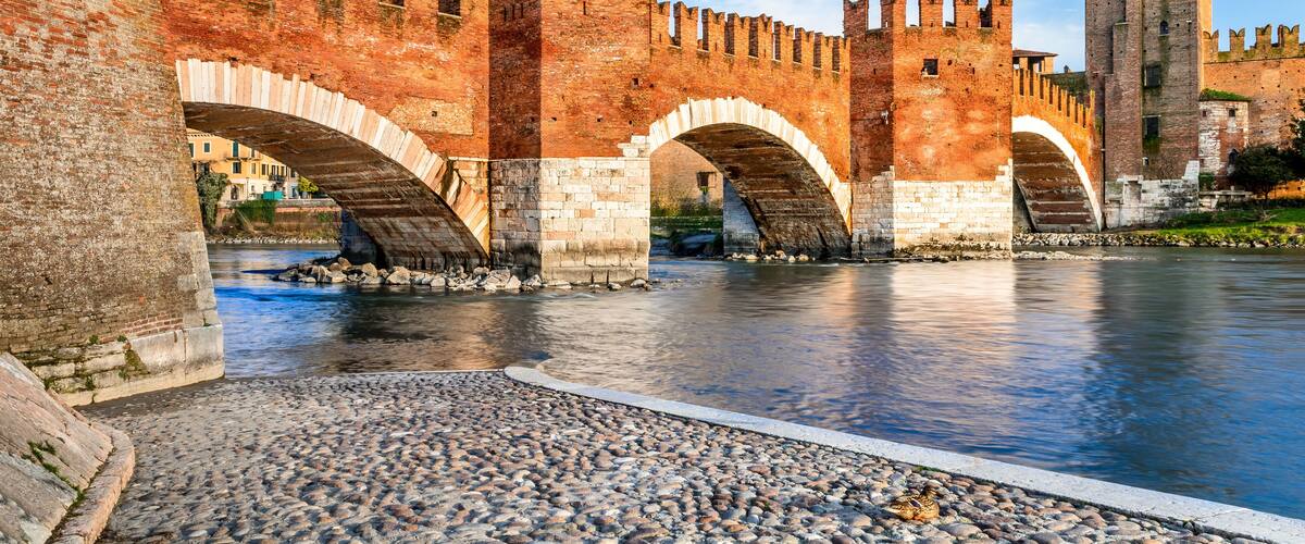 A historic stone bridge with arches over a river, surrounded by ancient brick walls and a tall tower.