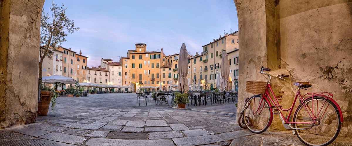 Una piazza aperta con pavimentazione in pietra, una bicicletta rossa e edifici storici sullo sfondo.