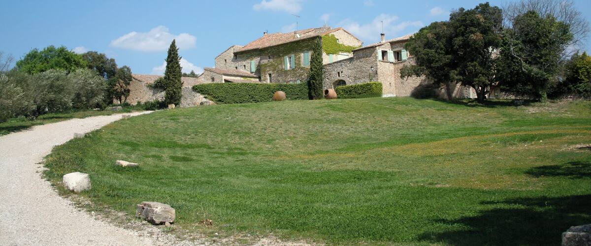A stone house with a tiled roof, surrounded by a grassy hill and trees.