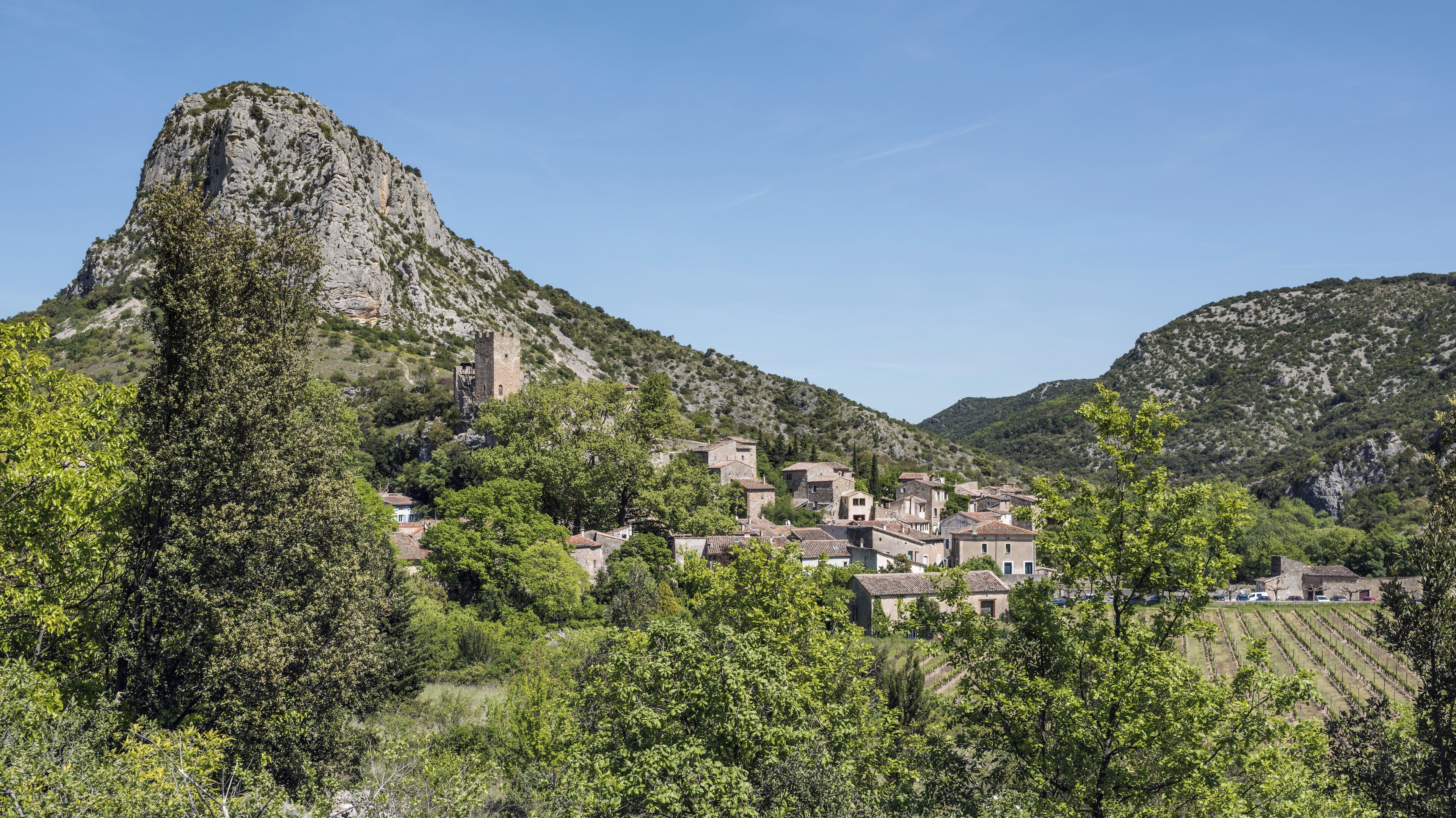 A village nestled in a valley with a prominent rocky hill and a tower.
