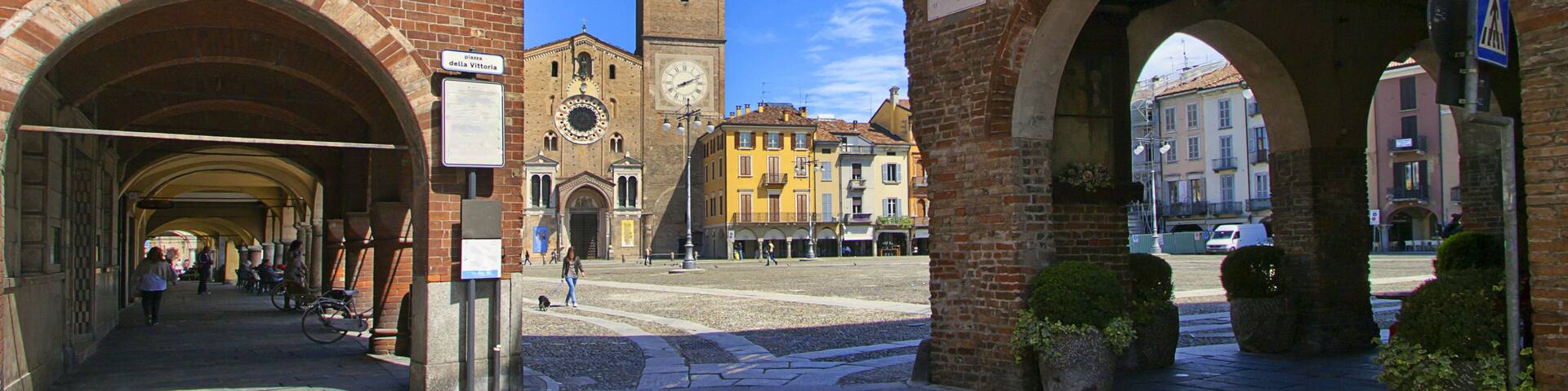 A historic square with brick buildings, a clock tower, and an archway.