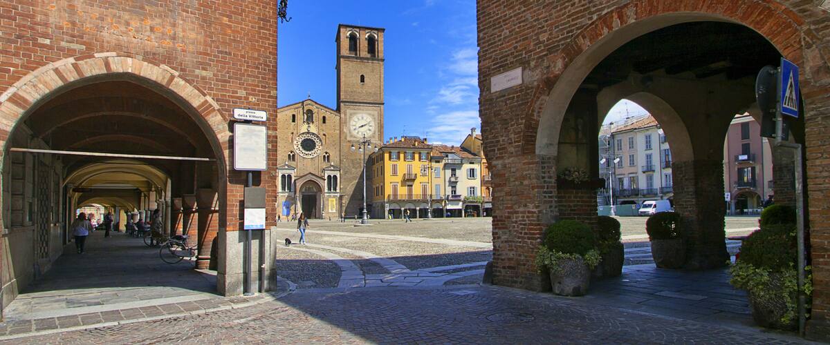 A historic square with brick buildings, a clock tower, and an archway.