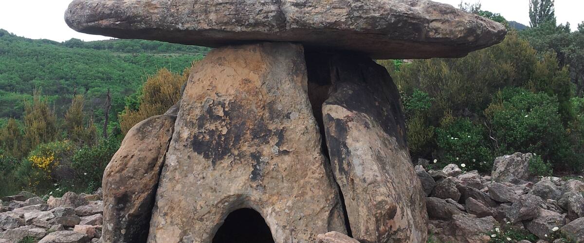 A mushroom-shaped stone structure with a cave entrance, surrounded by rocks and greenery.