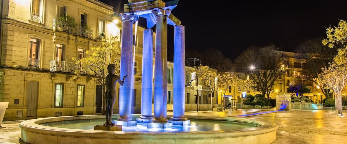 A night scene with a fountain featuring a statue and illuminated columns.