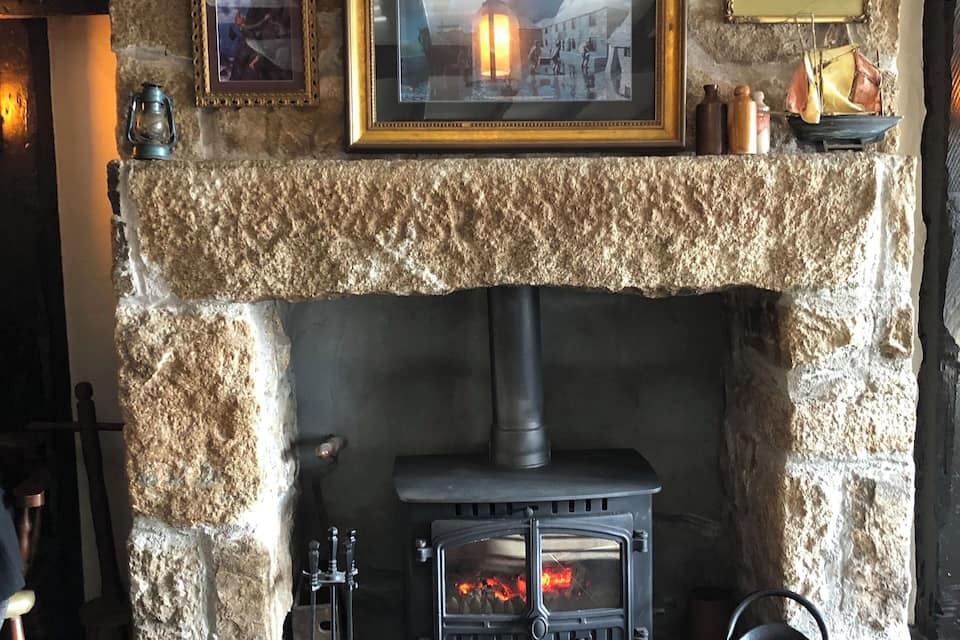 A stone fireplace with a wood-burning stove, framed pictures, and a hanging light fixture.