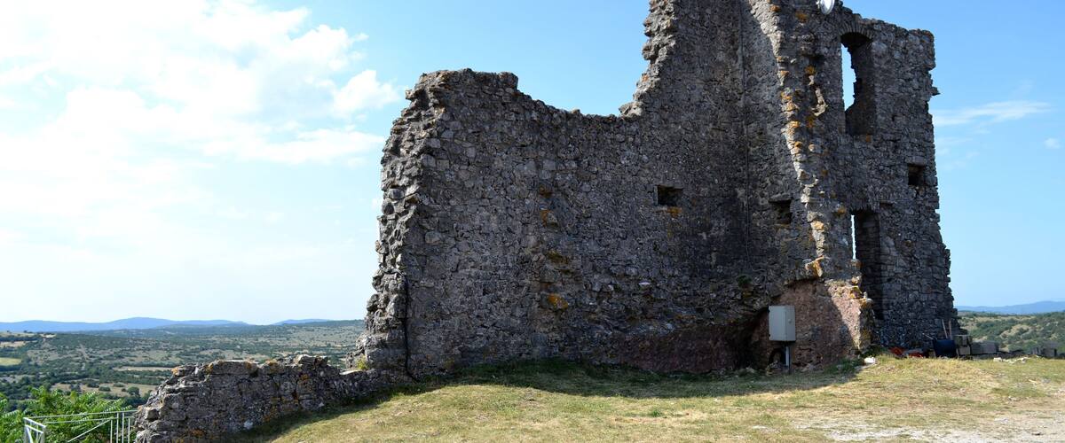 An ancient stone ruin with a partially intact tower, surrounded by grassy terrain and distant hills.