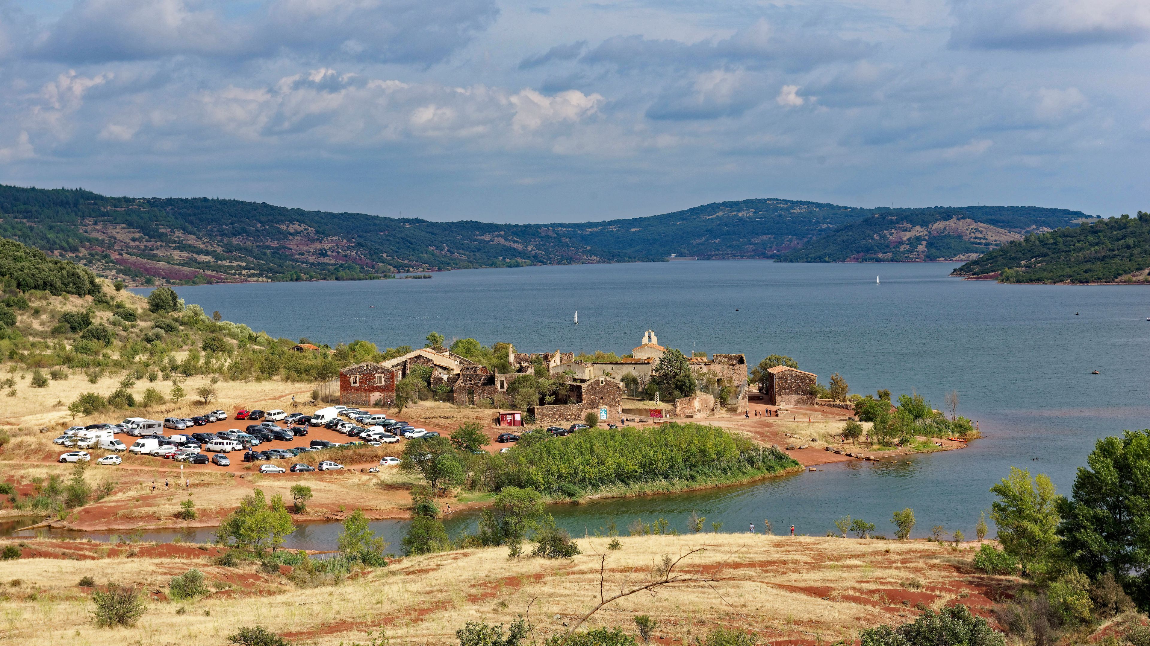 A lakeside village with historic buildings, a parking lot, and a distant sailboat.