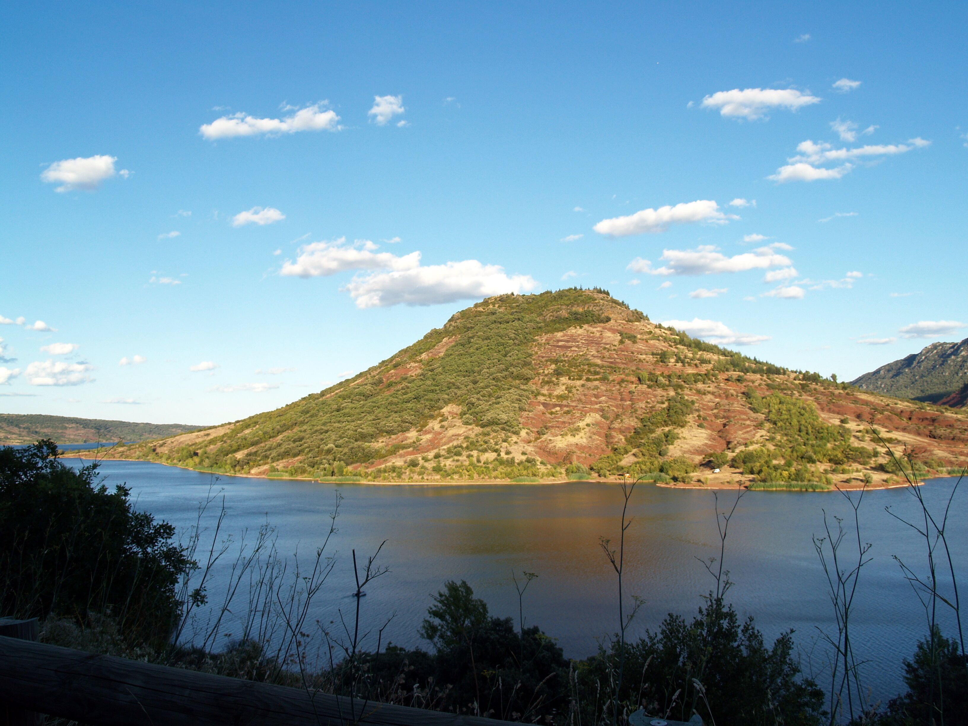 A lake surrounded by hills with sparse vegetation and a clear sky.