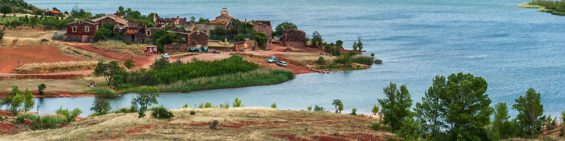 A coastal village with historic buildings by a large body of water, surrounded by hills.