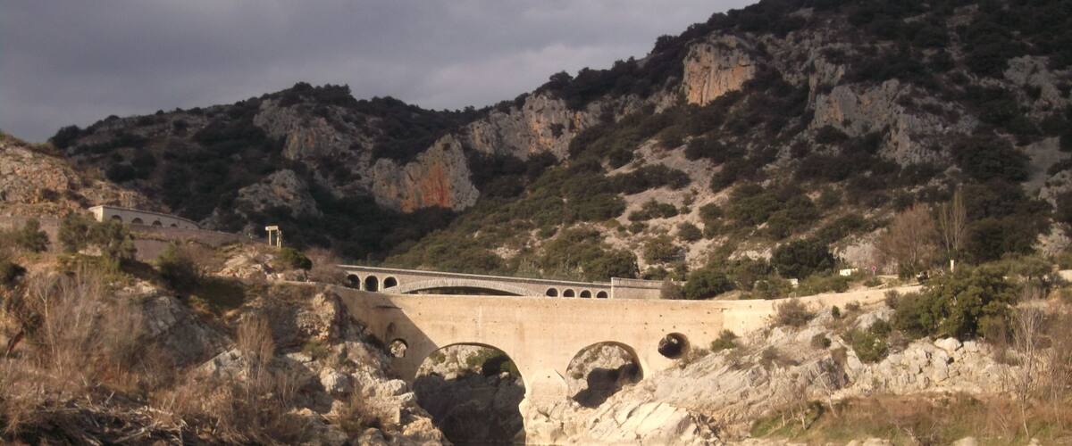 A stone bridge over a calm river, surrounded by rocky terrain and sparse vegetation.