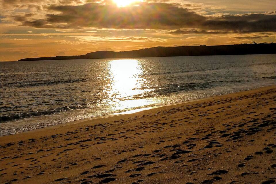 Uma praia com pegadas na areia e o sol se pondo sobre a água.