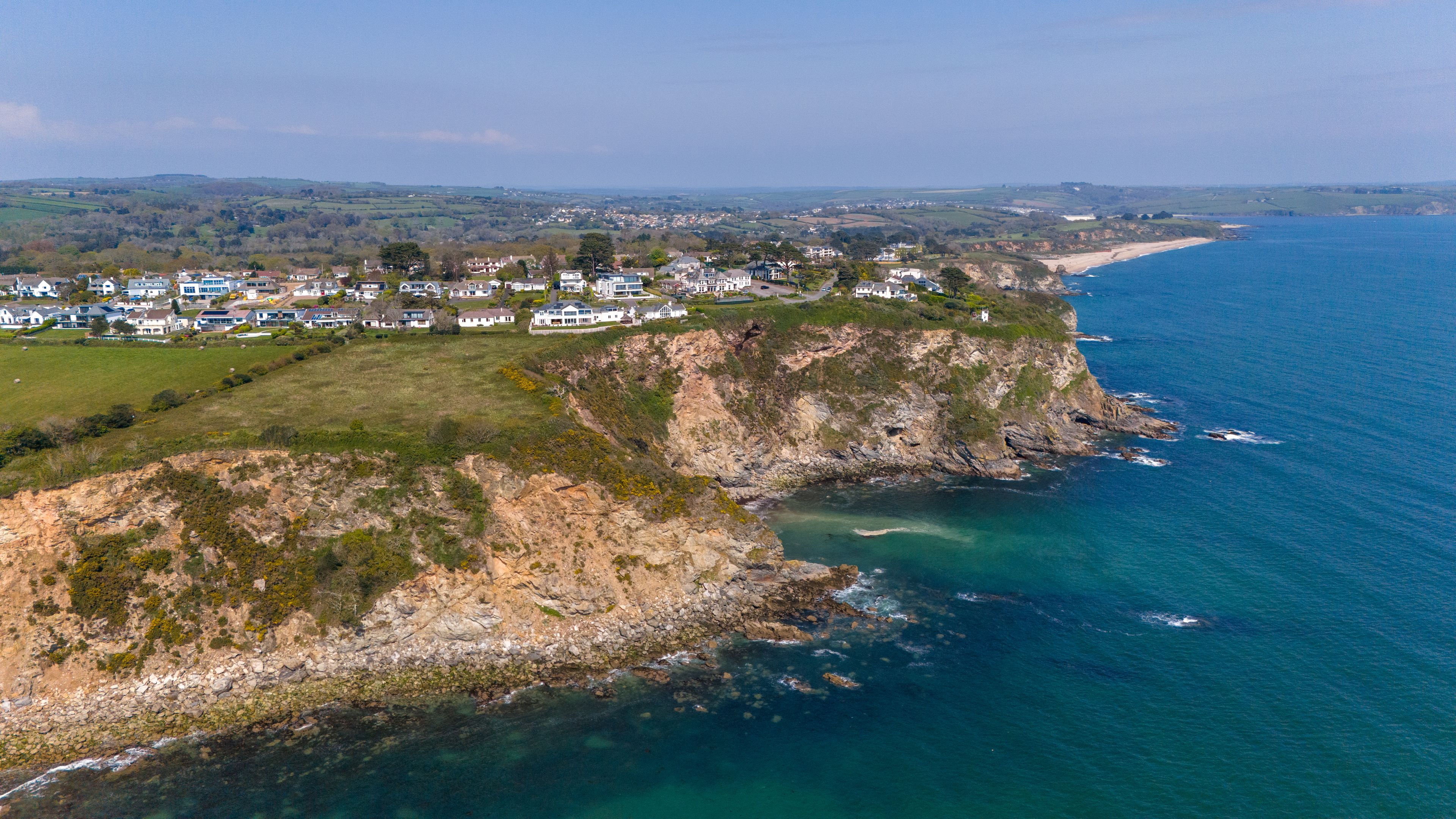 Aerial view of rugged cliffs meet the turquoise sea, with houses perched atop, a vibrant blend of nature and architecture., Carlyon Bay, Saint Austell, United Kingdom.
