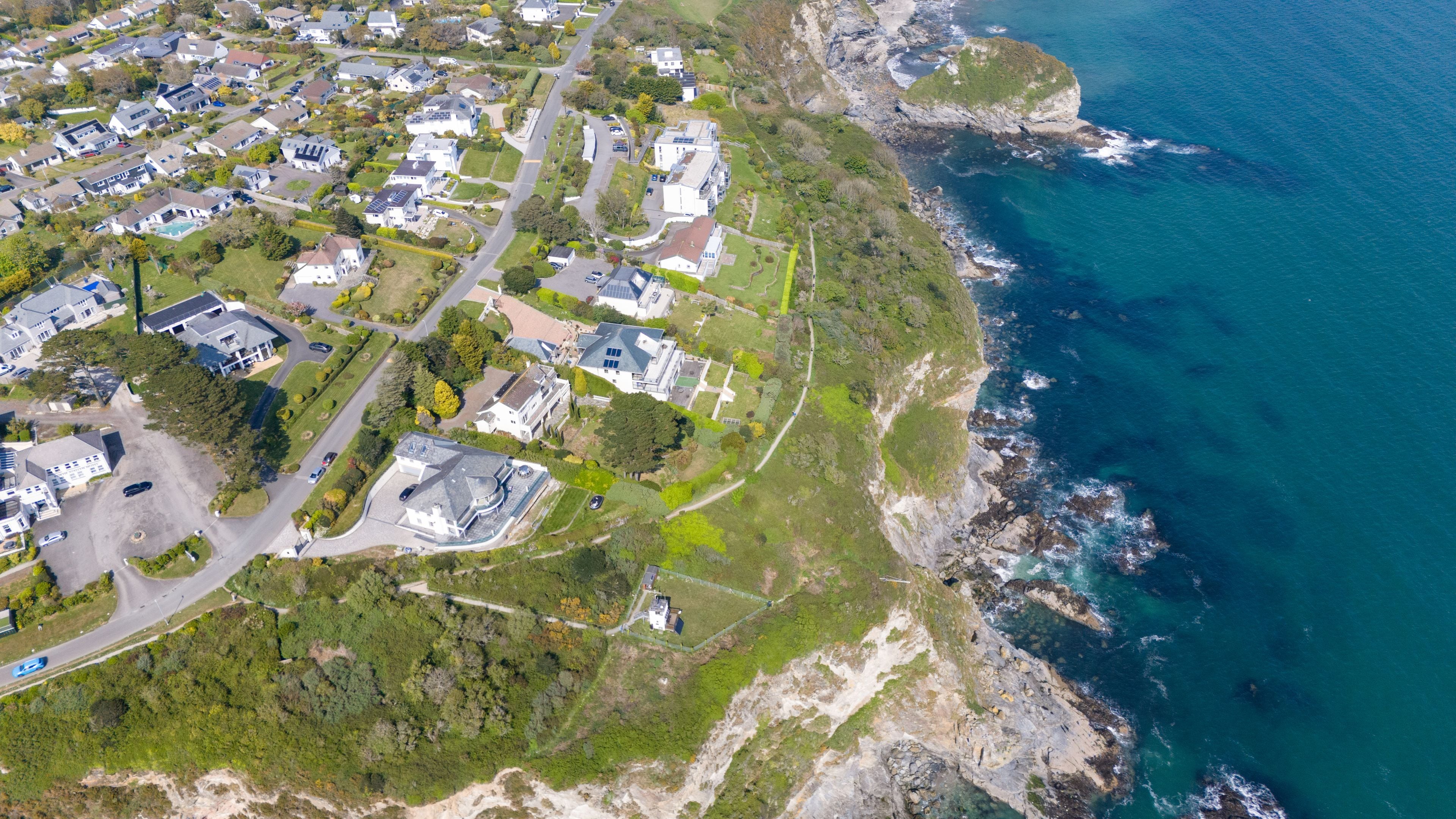 An aerial view of a coastal residential area with houses, roads, and a rocky coastline.