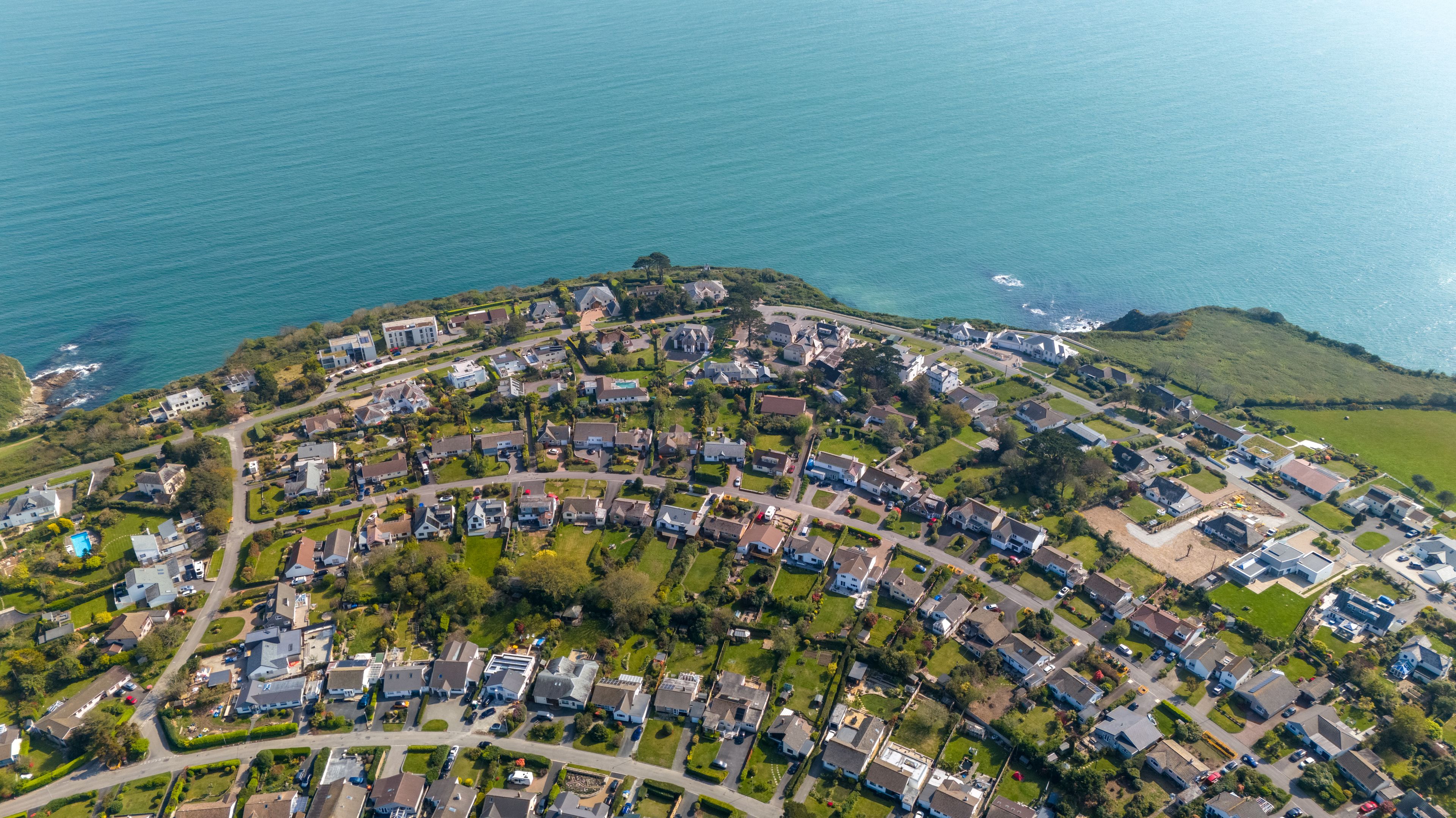 An aerial view of a coastal residential area with houses, roads, and a large body of water.