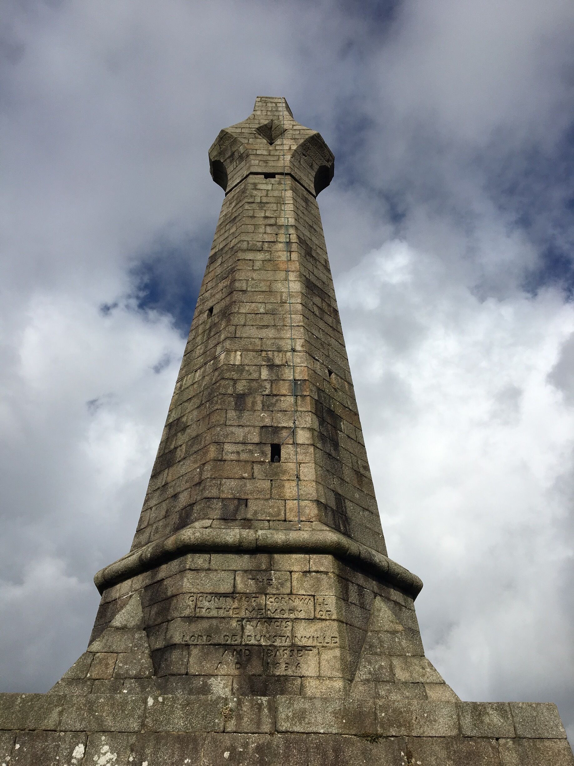 A stone tower with inscriptions, set against a cloudy sky.