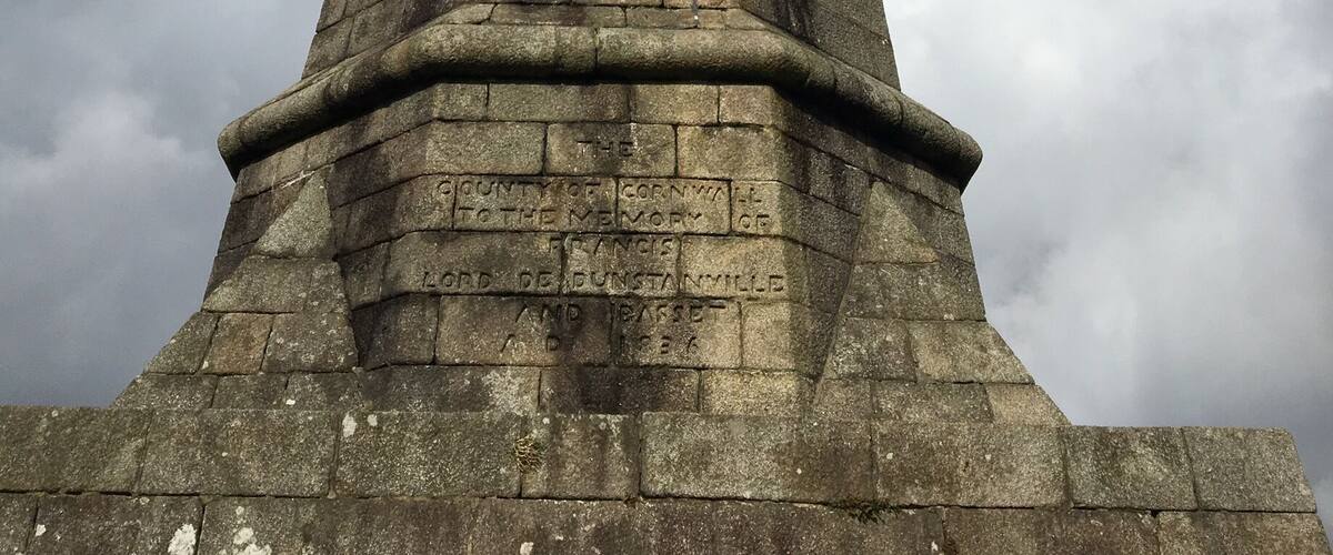 A stone tower with inscriptions, set against a cloudy sky.