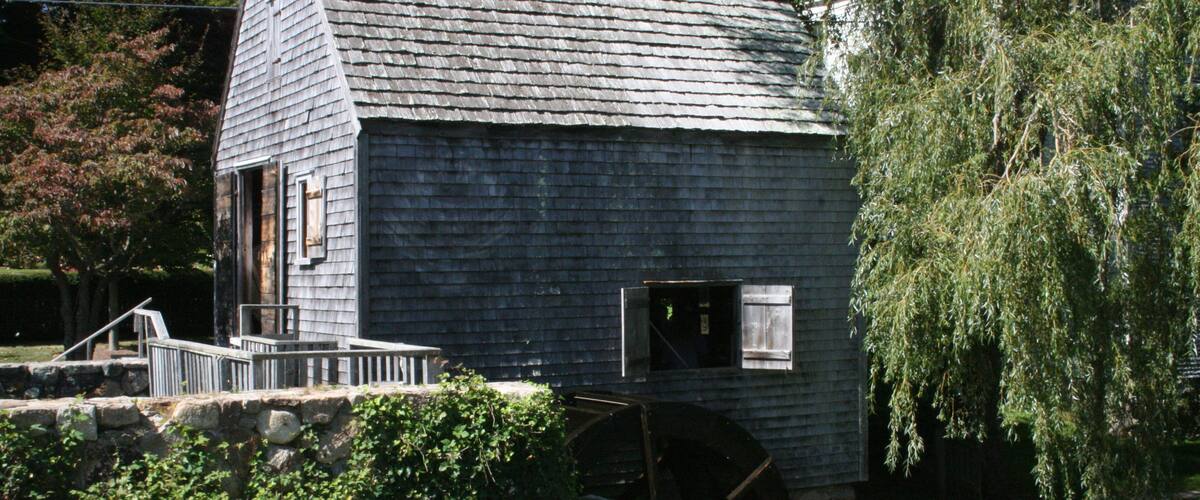 A rustic wooden building with a sloped roof and a large water wheel.