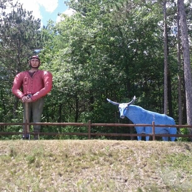 A person in a red jacket standing next to a blue bull statue in a grassy area with trees in the background.