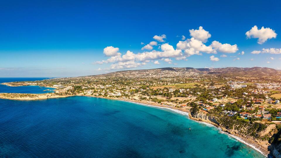 A coastal town with a beach, clear blue waters, and a mountainous backdrop.